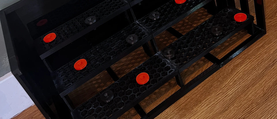 Black 3D printed 3 tier frag rack with red frag plugs on a wooden floor