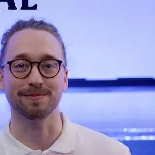 Harry from Marine Spec smiling in a white polo shirt in front of a blue lit reef tank