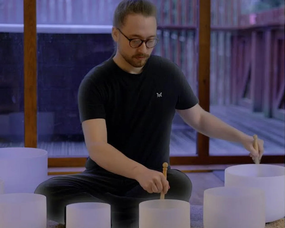 Harry sitting on a decking space playing crystal singing bowls