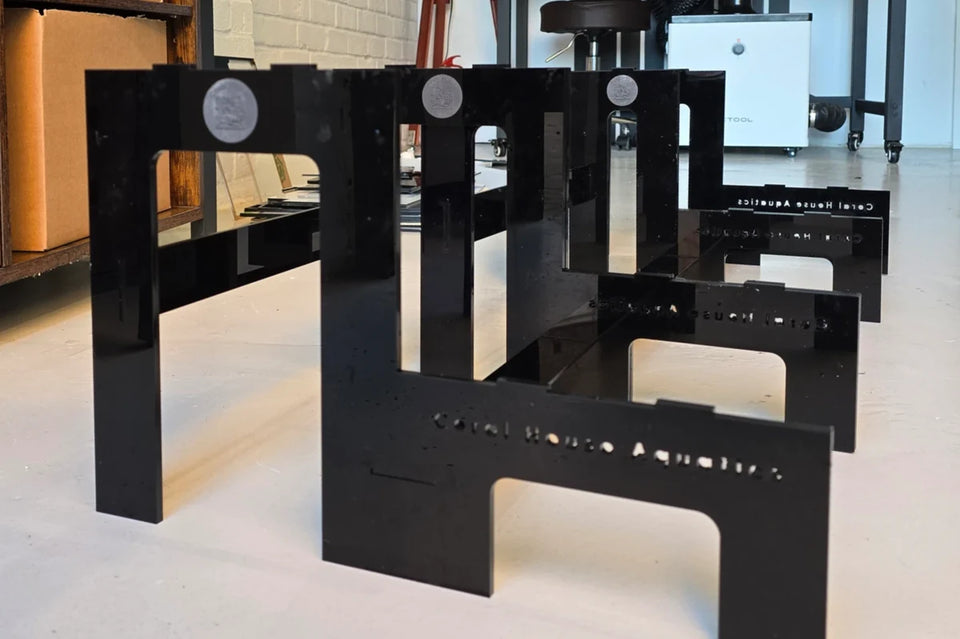 Black laser cut acrylic frag rack frames with engraved logos standing on a workshop floor
