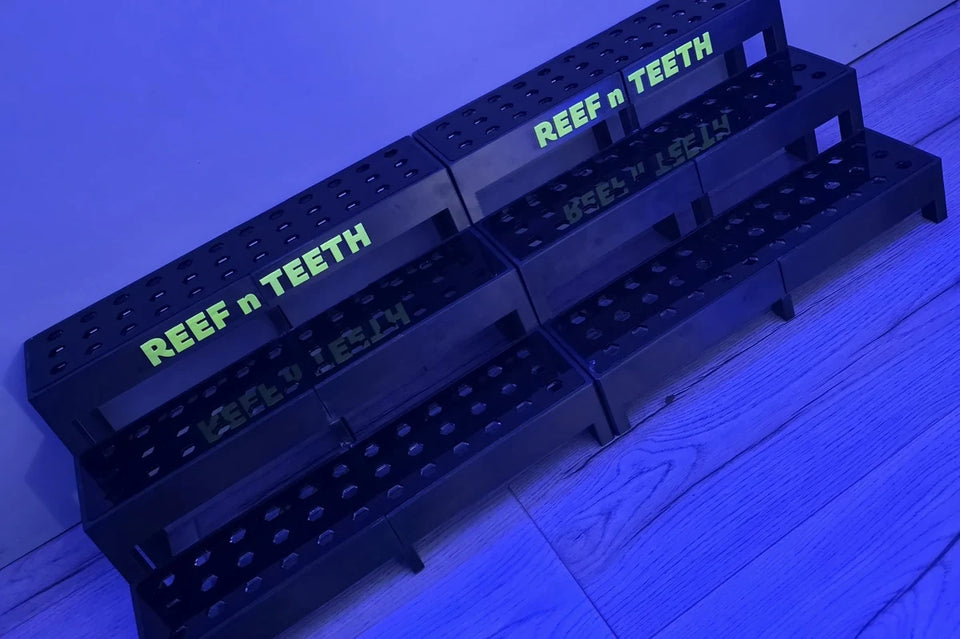 Black 3 tier hybrid frag rack with a bold yellow logo glowing under blue aquarium light