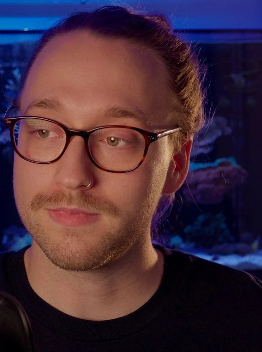 Harry from Marine Spec in a close up portrait, relaxed, with his lit reef tank behind him